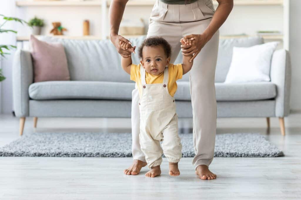 Cute african amerian toddler baby making first steps with mother's help
